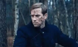 A Man In A Blue Jacket Is Standing In The Woods With Blood On His Face . GIF