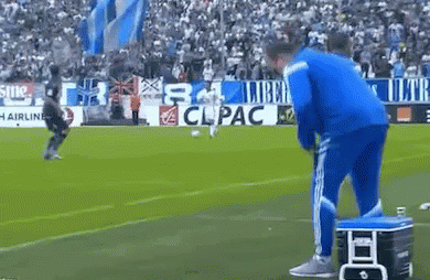 A Man In A Blue Jacket Is Standing On A Soccer Field Next To A Cooler .. GIF