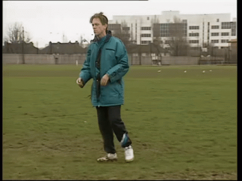 A Man In A Blue Jacket Is Walking On A Grassy Field GIF