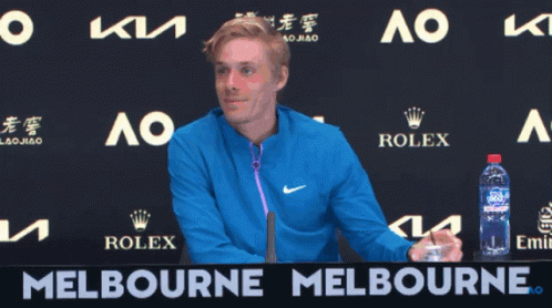 A Man In A Blue Jacket Stands In Front Of A Melbourne Banner GIF