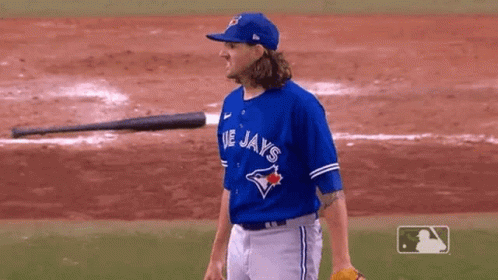 A Man In A Blue Jays Jersey Is Standing On A Baseball Field With A Bat In The Background . GIF