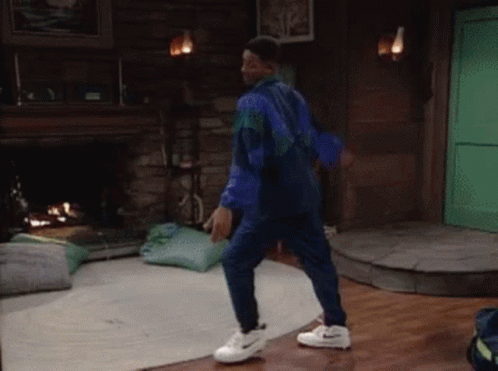 A Man In A Blue Jumpsuit And White Nike Shoes Is Dancing In A Living Room GIF