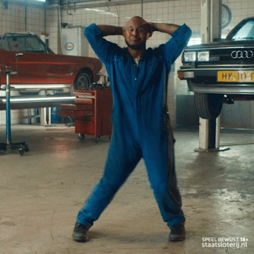 A Man In A Blue Jumpsuit Is Dancing In Front Of An Audi Car GIF