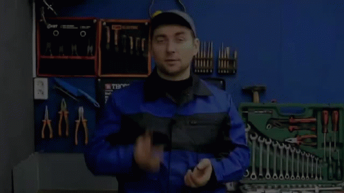 A Man In A Blue Jumpsuit Is Standing In Front Of A Toolbox Filled With Tools . GIF