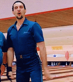 A Man In A Blue Jumpsuit Is Standing On A Bowling Alley GIF
