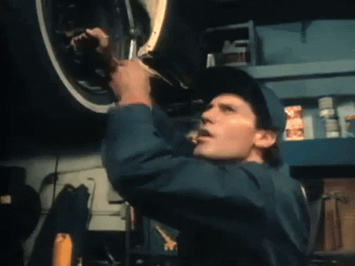 A Man In A Blue Jumpsuit Is Working On A Car GIF