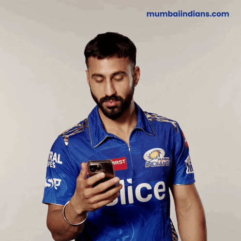 A Man In A Blue Mumbai Indians Jersey Looks At His Cell Phone GIF
