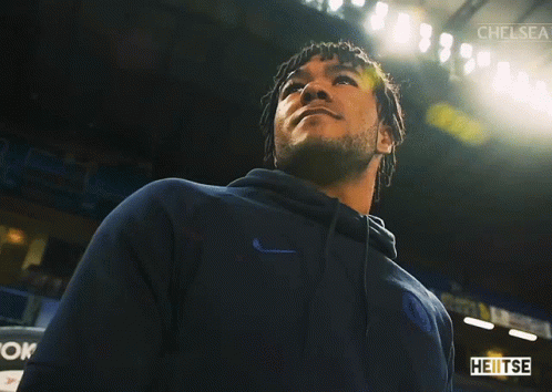 A Man In A Blue Nike Hoodie Stands In A Dark Room With Chelsea Written On The Bottom GIF