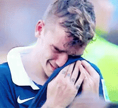 A Man In A Blue Nike Shirt Is Crying With His Hands On His Face . GIF