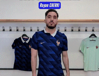 A Man In A Blue Nike Shirt Is Standing In Front Of A Sign That Says Rayan Cherki GIF
