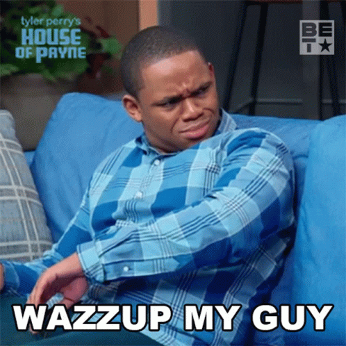 A Man In A Blue Plaid Shirt Is Sitting On A Blue Couch With The Words Wazzup My Guy Above Him GIF