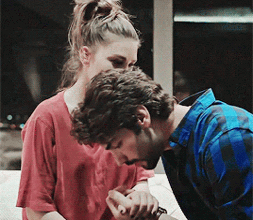 A Man In A Blue Plaid Shirt Kisses A Woman On The Cheek GIF
