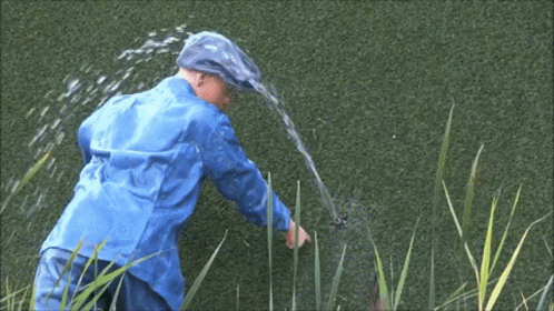 A Man In A Blue Raincoat Is Spraying Water From A Hose . GIF