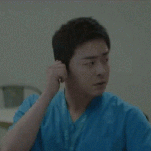 A Man In A Blue Scrub Is Adjusting His Ear Buds GIF