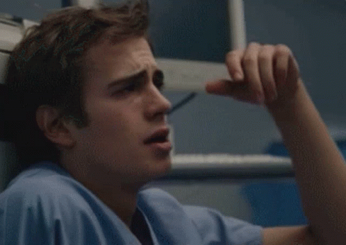 A Man In A Blue Scrub Top Is Holding His Head GIF
