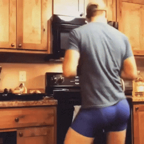 A Man In A Blue Shirt And Blue Shorts Is Standing In A Kitchen Cooking . GIF