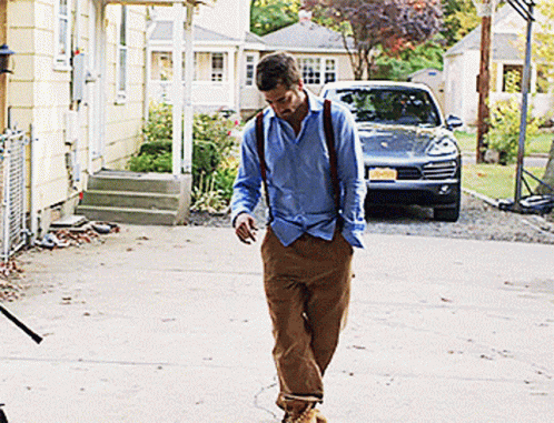 A Man In A Blue Shirt And Brown Pants Is Walking In Front Of A Car With A License Plate That Says N.j. GIF