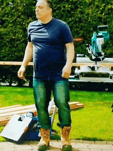 A Man In A Blue Shirt And Jeans Is Standing On A Sidewalk GIF