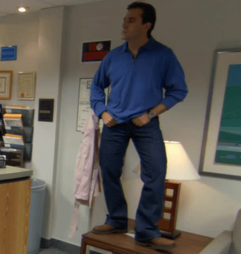 A Man In A Blue Shirt And Jeans Stands On A Table GIF
