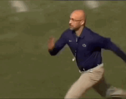 A Man In A Blue Shirt And Khaki Pants Is Running Across A Field . GIF