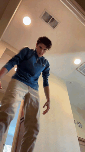 A Man In A Blue Shirt And Khaki Pants Is Standing In A Doorway GIF