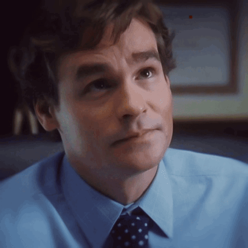 A Man In A Blue Shirt And Polka Dot Tie Looks To The Side GIF