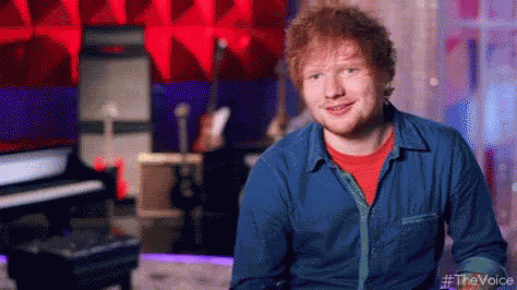 A Man In A Blue Shirt And Red T-Shirt Is Smiling In A Recording Studio . GIF