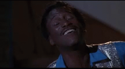A Man In A Blue Shirt And Silver Vest Is Smiling With His Eyes Closed . GIF