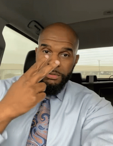 A Man In A Blue Shirt And Tie Holds His Finger Up To His Nose GIF