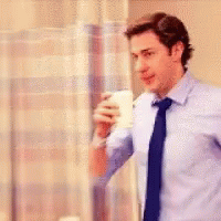 A Man In A Blue Shirt And Tie Is Holding A Cup Of Coffee In A Hospital Room . GIF