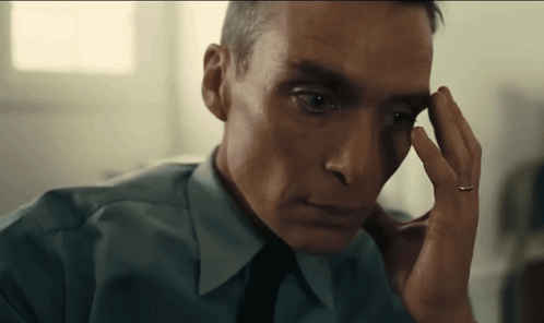 A Man In A Blue Shirt And Tie Is Holding His Hand To His Forehead . GIF