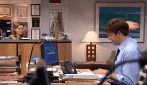 A Man In A Blue Shirt And Tie Is Sitting At A Desk In An Office . GIF