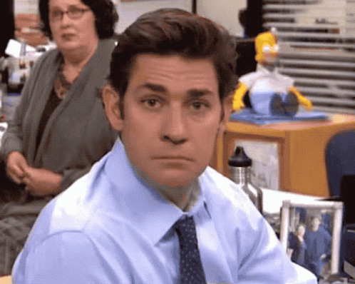 A Man In A Blue Shirt And Tie Is Sitting At A Desk In An Office GIF