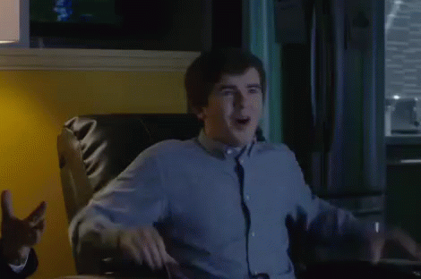 A Man In A Blue Shirt And Tie Is Sitting In A Chair And Making A Funny Face . GIF