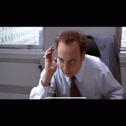 A Man In A Blue Shirt And Tie Is Sitting In Front Of A Computer GIF