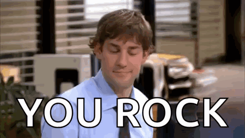 A Man In A Blue Shirt And Tie Is Sitting In Front Of A Sign That Says You Rock . GIF