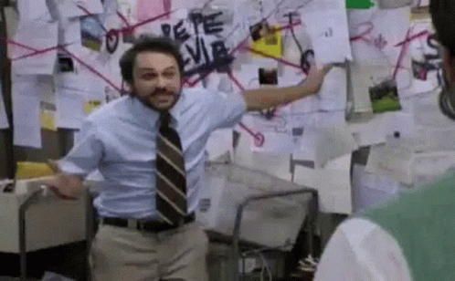 A Man In A Blue Shirt And Tie Is Standing In Front Of A Wall With Papers On It . GIF