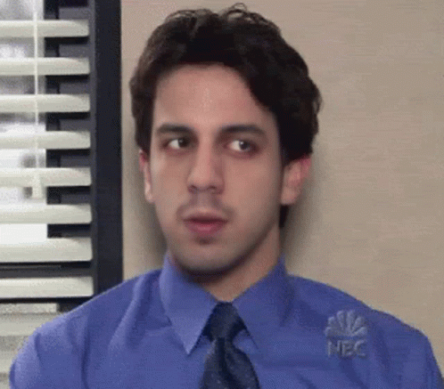 A Man In A Blue Shirt And Tie Is Standing In Front Of A Window With Blinds . GIF