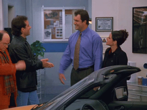A Man In A Blue Shirt And Tie Is Standing Next To A Woman In A Black Coat GIF