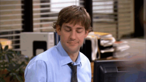 A Man In A Blue Shirt And Tie Sitting In Front Of A Computer Monitor GIF