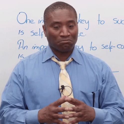 A Man In A Blue Shirt And Tie Stands In Front Of A White Board With The Words One In Key To Self Written On It GIF