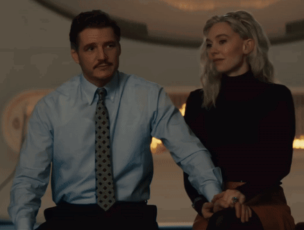 A Man In A Blue Shirt And Tie Stands Next To A Woman In A Black Turtleneck GIF