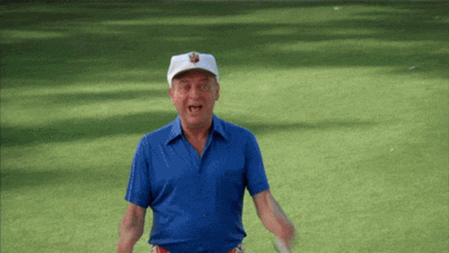 A Man In A Blue Shirt And White Hat Is Holding A Golf Club On A Golf Course GIF