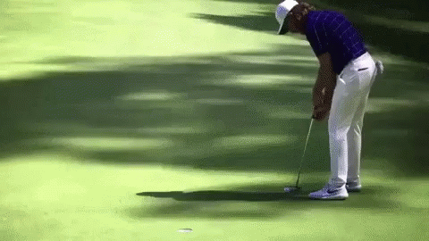 A Man In A Blue Shirt And White Pants Is Putting A Golf Ball GIF