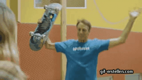 A Man In A Blue Shirt Holding A Skateboard With Gif-Erstellen.com Written On The Bottom GIF