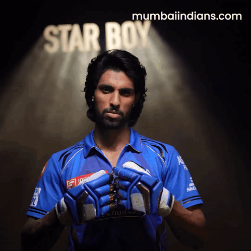 A Man In A Blue Shirt Holds His Gloves In Front Of A Star Boy Sign GIF