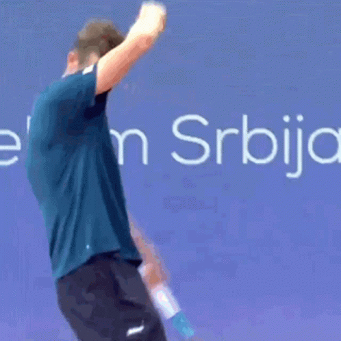 A Man In A Blue Shirt Is Bending Over In Front Of A Sign That Says Elek S. GIF