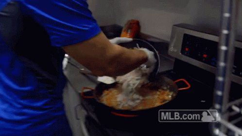 A Man In A Blue Shirt Is Cooking In A Kitchen With A Mlb.com Logo On The Stove GIF