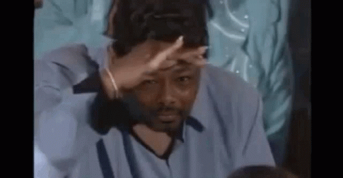 A Man In A Blue Shirt Is Covering His Face With His Hand While Sitting At A Table . GIF