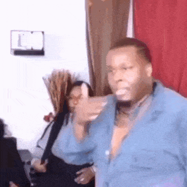 a man in a blue shirt is dancing in a living room with a woman in the background .